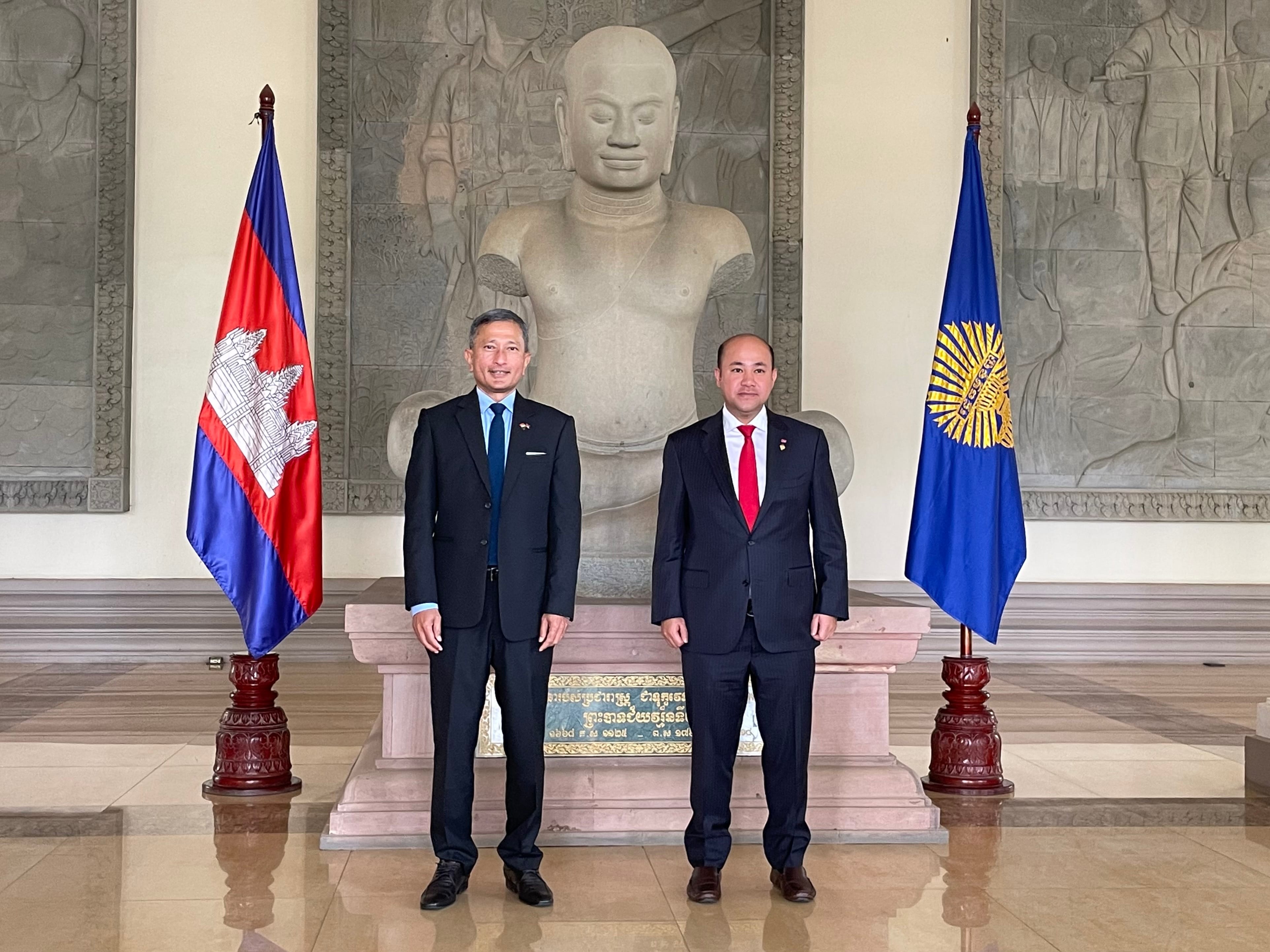 Two men in suits stand before flags of Cambodia and ASEAN with a Buddha statue behind.